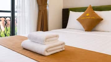 A neatly made bed with white linens and a brown headboard, a pillow with a logo, and a window with curtains.