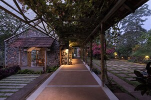 A stone building with a covered walkway, potted plants, and a paved path.