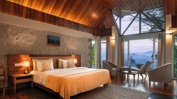 Un dormitorio amplio con una cama grande, techo de madera y vistas a montañas a través de ventanas grandes.