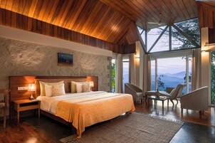 Un dormitorio amplio con una cama grande, techo de madera y vistas a montañas a través de ventanas grandes.