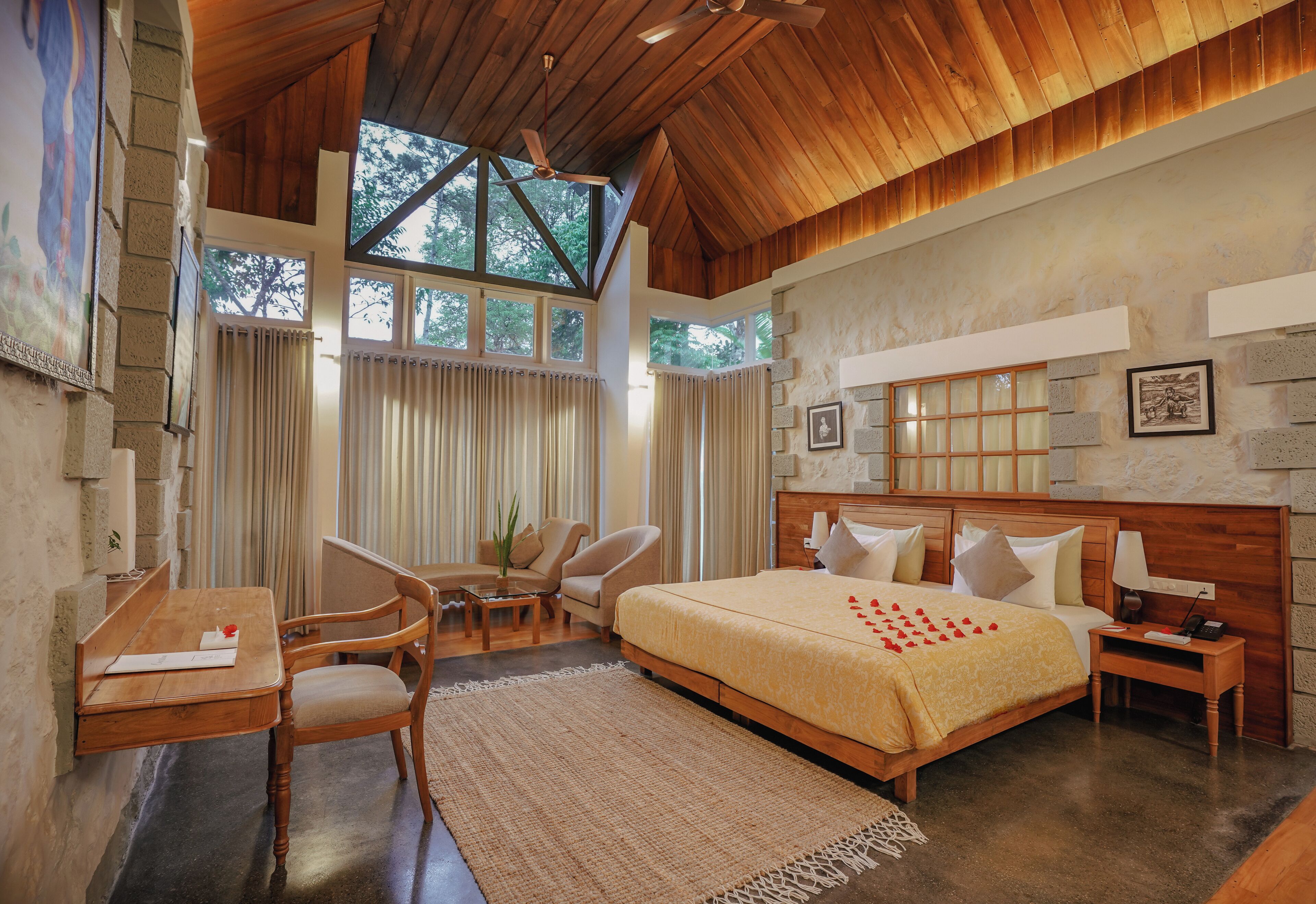 Amplia habitación con una cama grande, cabecera de madera y vistas a árboles a través de grandes ventanales.