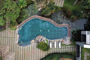 An aerial view of a swimming pool surrounded by a stone border, with a small garden area and lounge chairs.