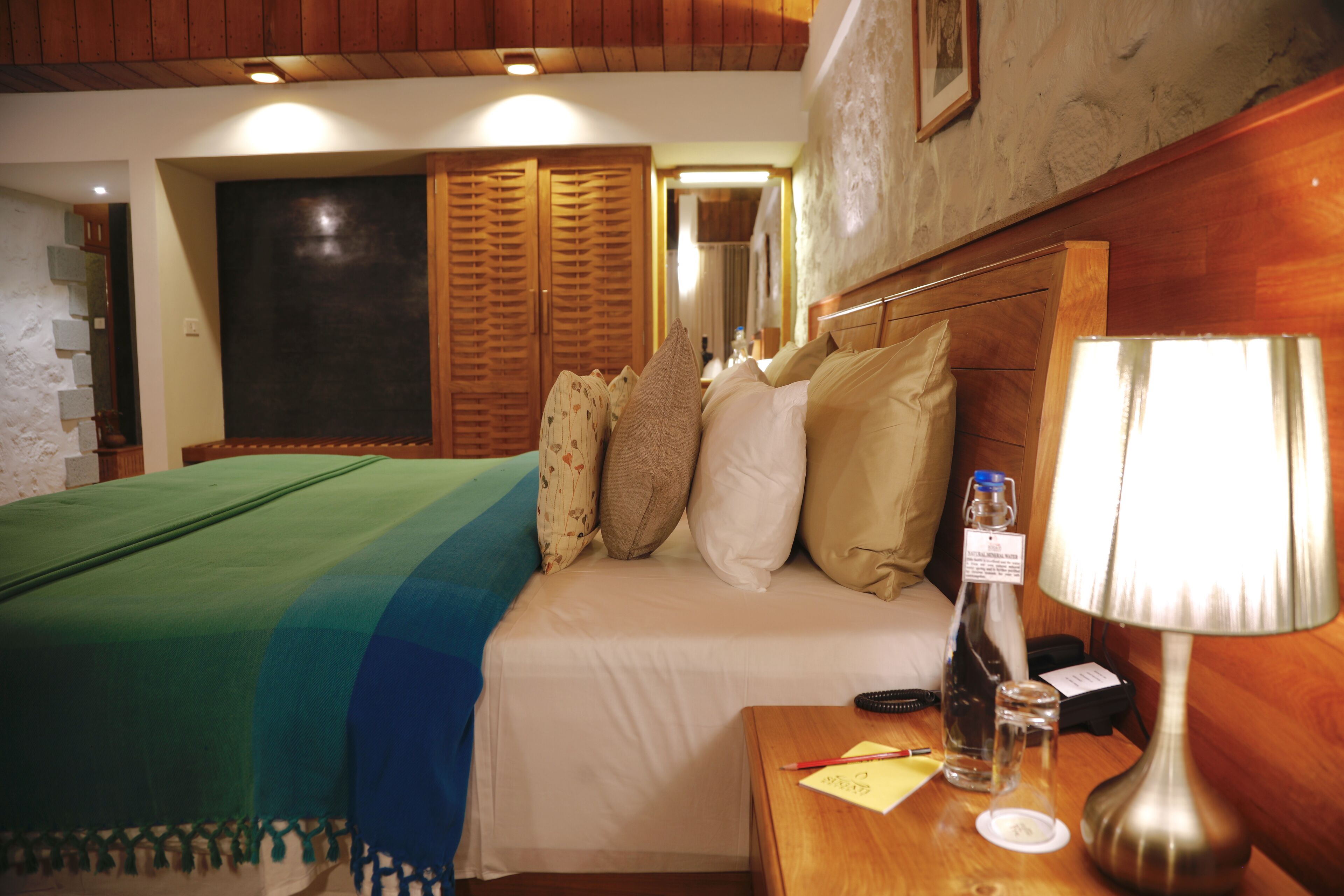 Ein Hotelzimmer mit einem Bett, einem Nachttisch mit Lampe, einer Flasche und einer Fernbedienung.