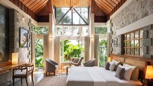 A spacious bedroom with a large bed, two armchairs, a desk, and a view of lush greenery through large windows. - SpiceTree Rajakumari (Udumbanchola)