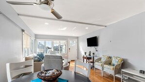 A modern living room with a dining table, chairs, a sofa, and a television on the wall.
