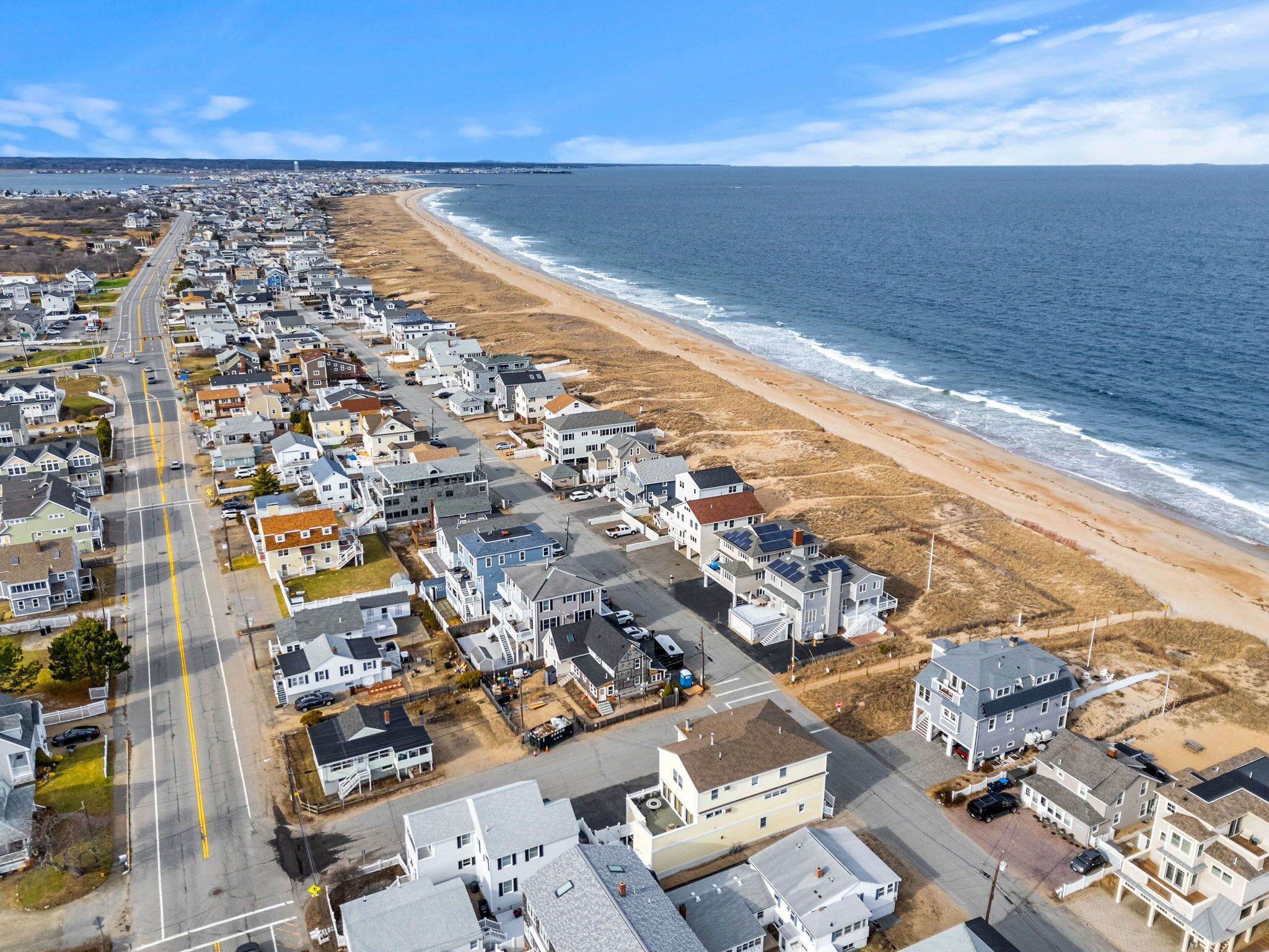 A coastal residential area with houses along the beach, a clear road, and the ocean in the background.