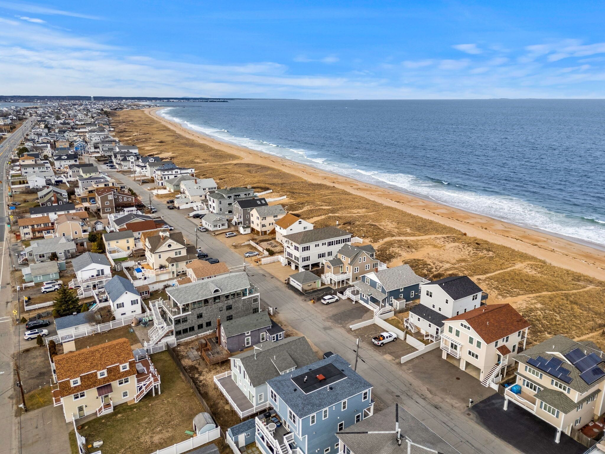 A coastal residential area with houses along the beach, a road, and a view of the ocean.