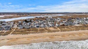 A coastal residential area with houses along the beachfront, a sandy beach, and a body of water in the background.
