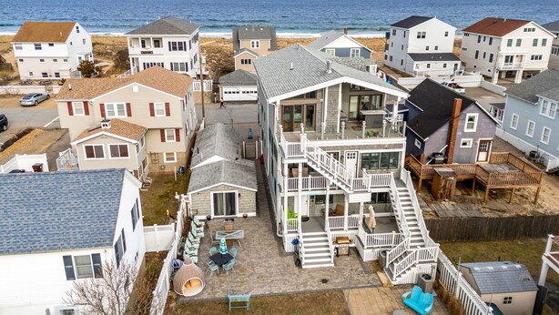 A coastal residential area with multiple houses, a large two-story building with a balcony, and a view of the ocean.