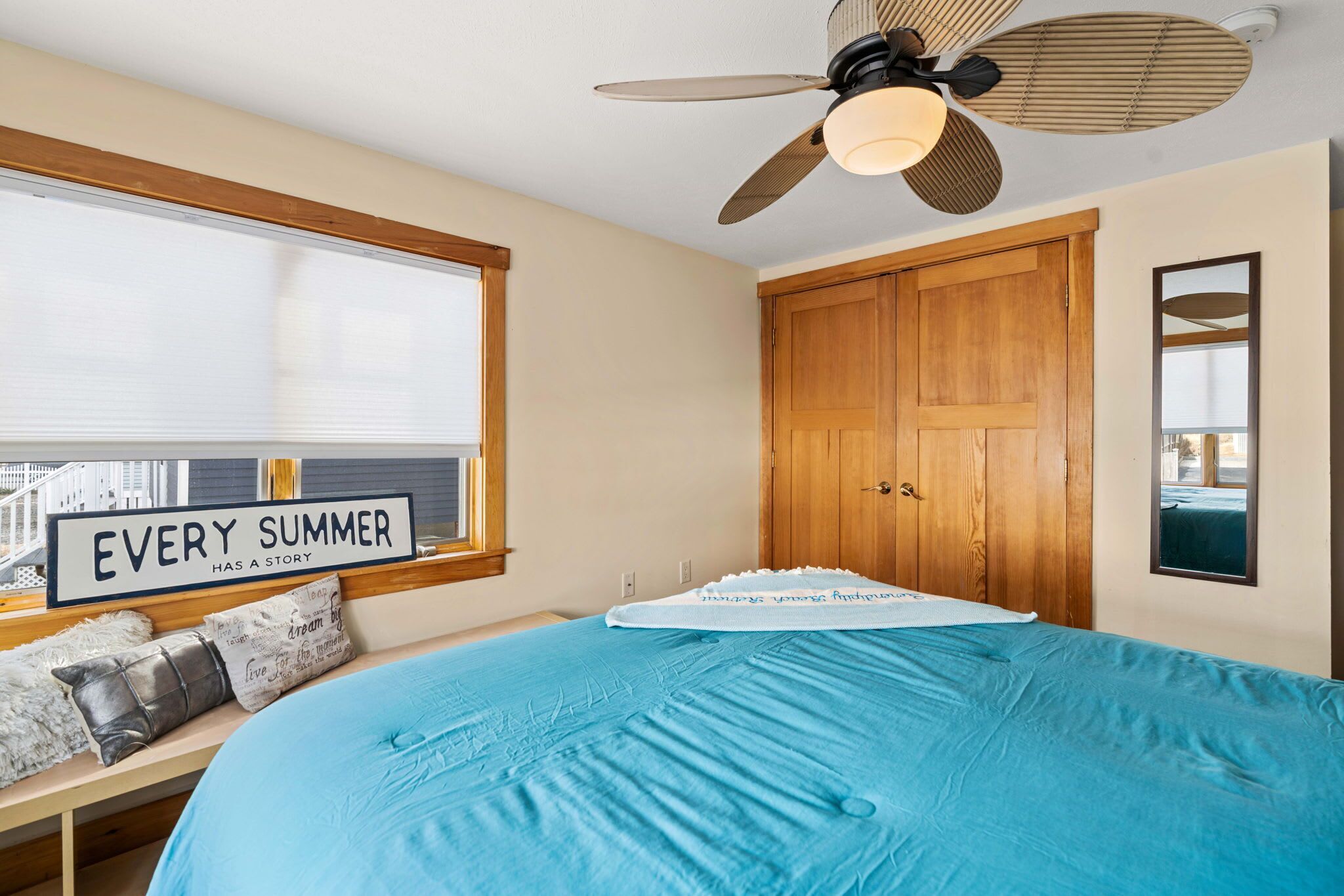 A bedroom with a bed, a ceiling fan, a window with blinds, and a wooden wardrobe.