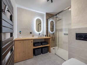 Ein modernes Badezimmer mit Waschtisch aus Holz, einer Duschkabine aus Glas und einem großen Spiegel mit integrierter Beleuchtung.