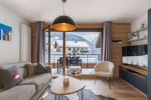 A modern living room with a sofa, a coffee table, and a TV. There is a large window with a view of snow-covered houses and mountains. - ART MONY 203 (CHATEL)