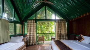 A room with two beds, a wooden floor, a balcony with a chair, and a view of greenery outside. - Gorukana Eco Wellness Centre (Yelandur)
