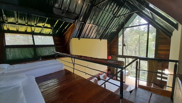 Una habitación con techo inclinado, suelo de madera, cama, mesa y vistas al exterior a través de amplios ventanales.