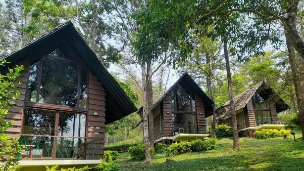 A row of wooden cabins with large windows, surrounded by lush greenery and trees. - Gorukana Eco Wellness Centre (Yelandur)