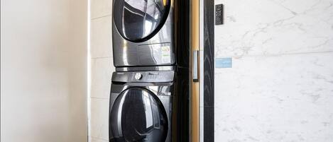 Un appareil combiné lave-linge et sèche-linge fixé au mur, placé dans un coin, avec un mur en marbre et une porte.