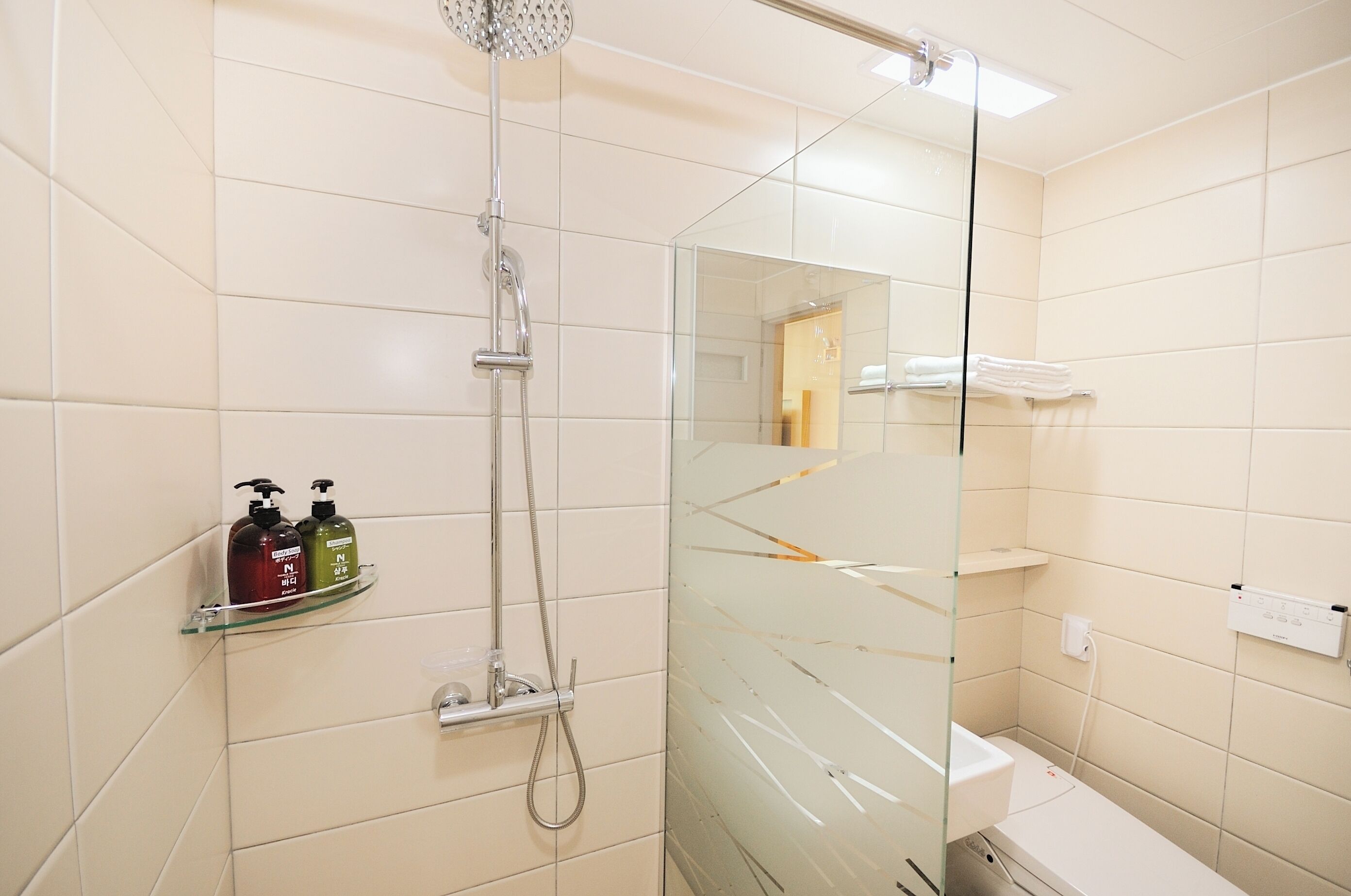 A modern bathroom with a glass shower enclosure, a glass shelf with toiletries, and a white tiled wall.