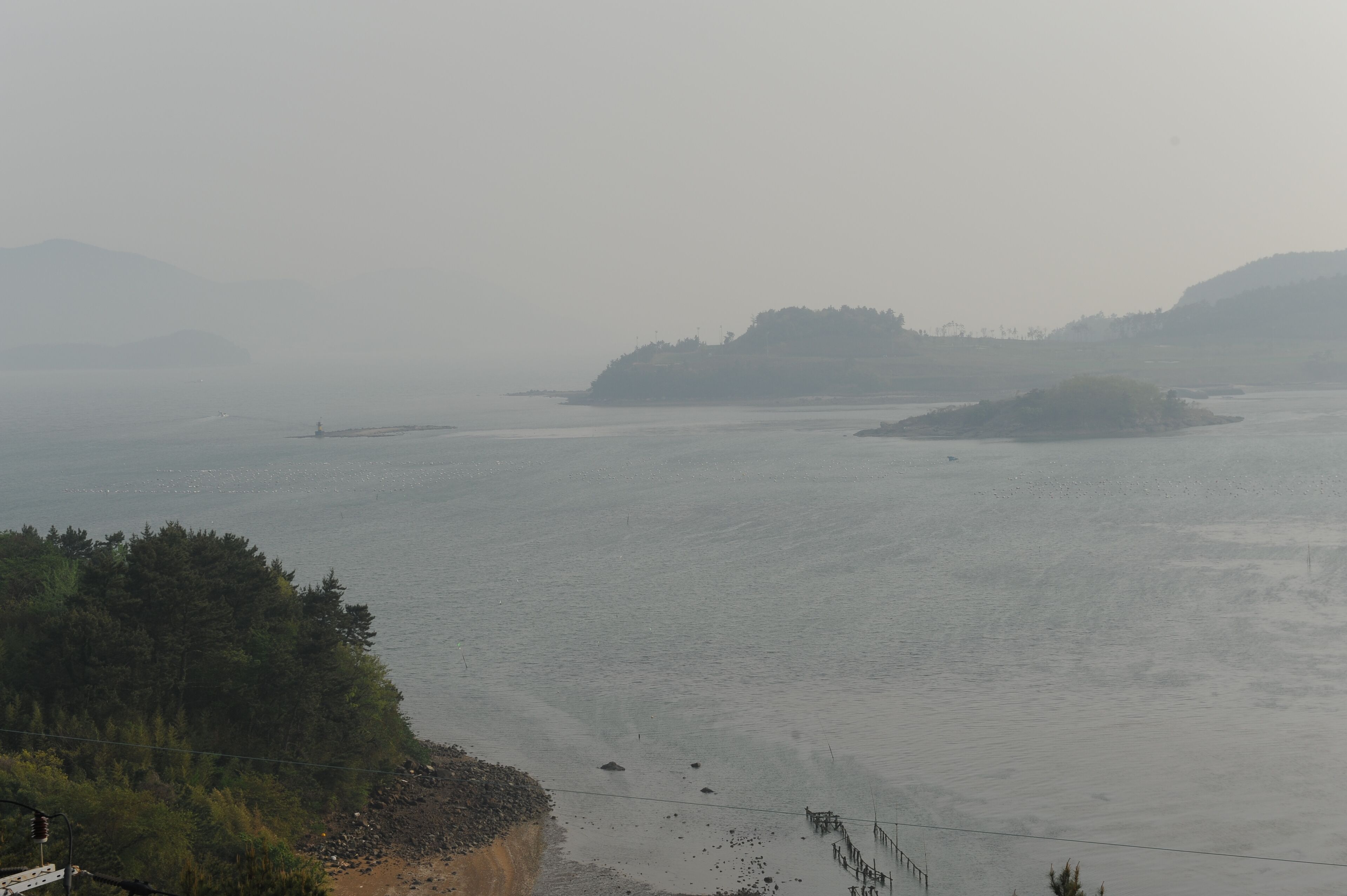 Paisaje costero con agua tranquila, un faro y islas a la distancia.