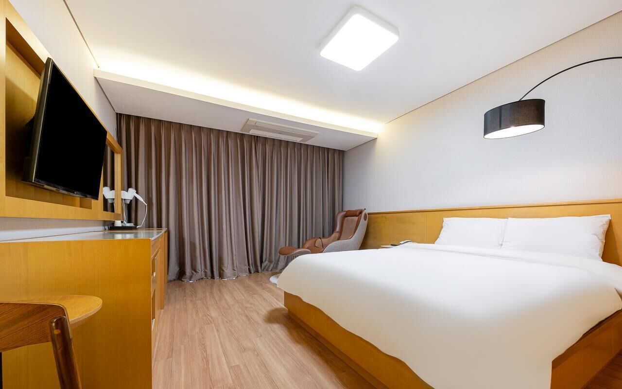 Quarto de hotel com cama, escrivaninha, cadeira, televisão e luminária de teto.