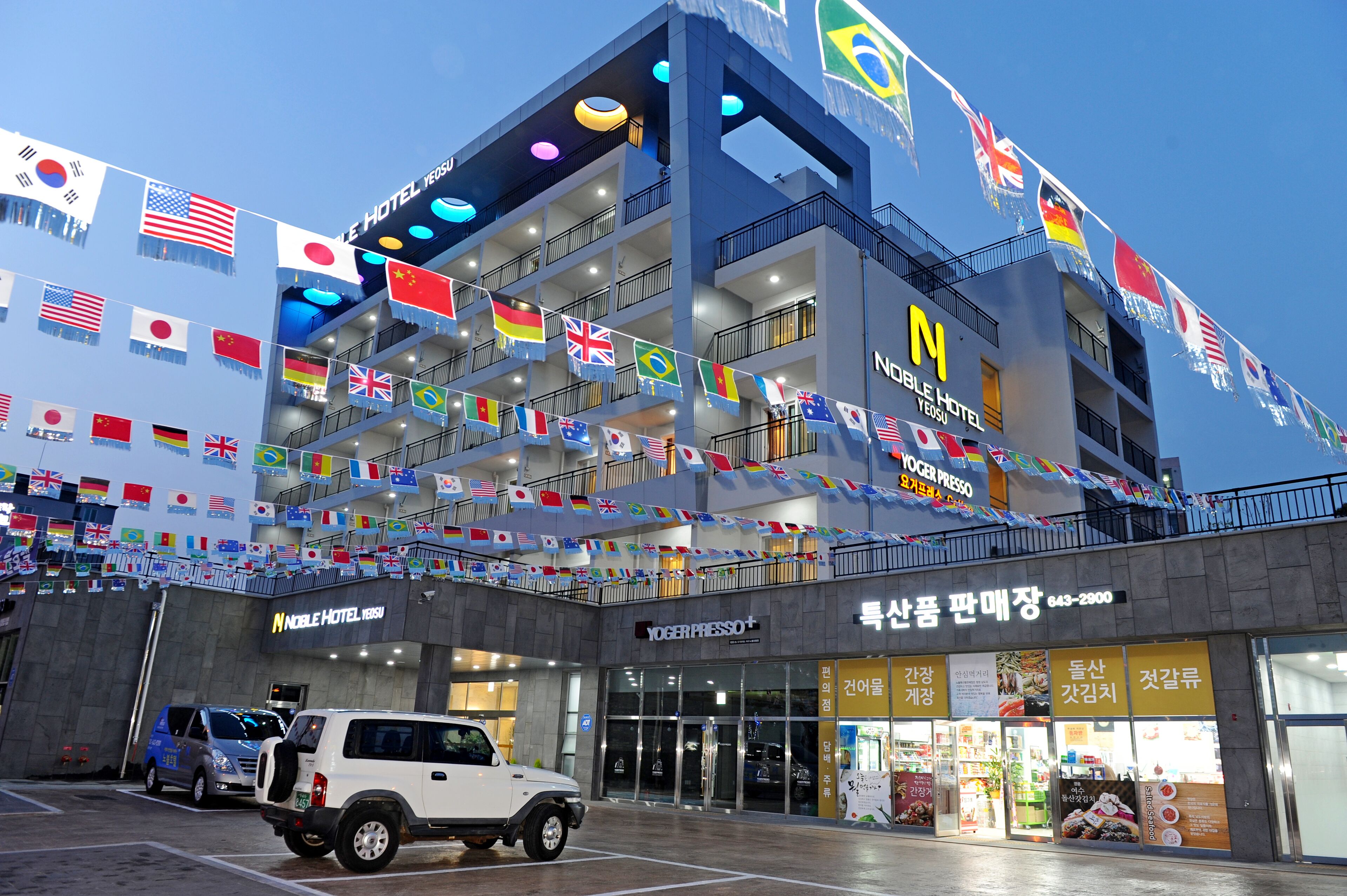 A multi-story hotel with balconies, a mobile press office, and various flags.