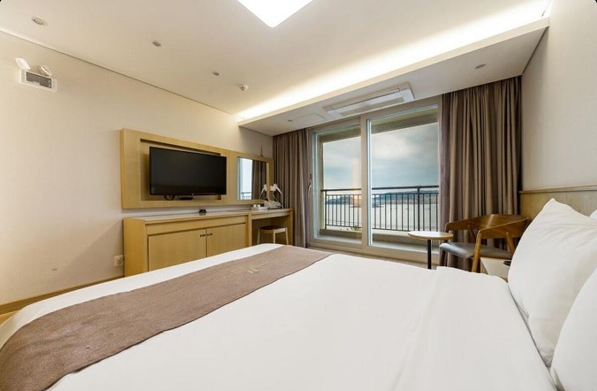 Habitación de hotel con una cama grande, un escritorio con televisión de pantalla plana, una silla y un balcón con cortinas.
