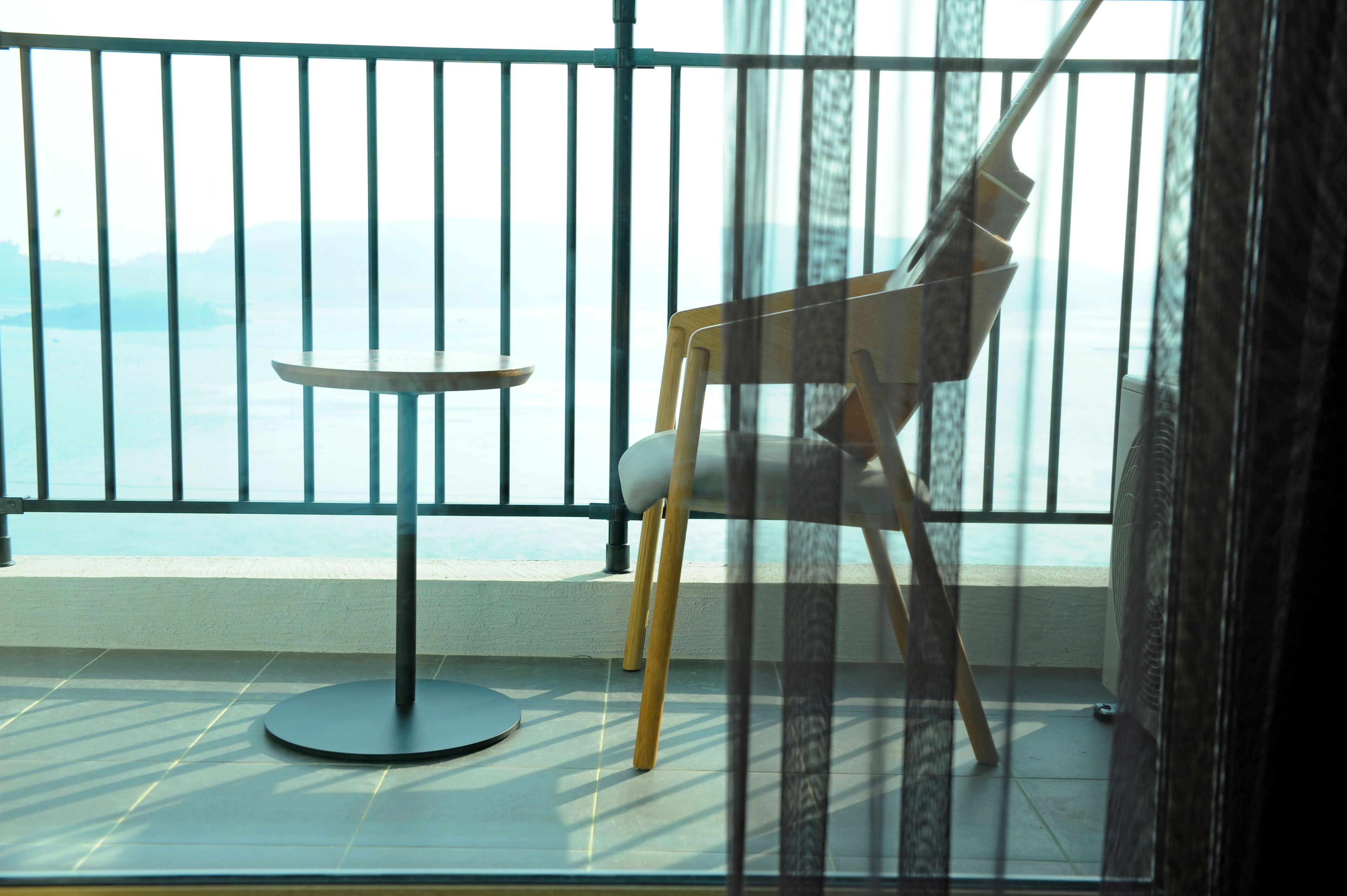 A balcony with a chair and a small table, overlooking a body of water.
