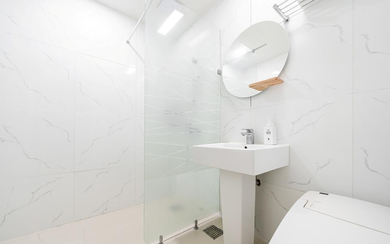 Un baño moderno con cabina de ducha de vidrio, un lavabo blanco y un espejo con repisa de madera.