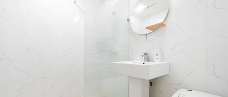 Un baño moderno con cabina de ducha de vidrio, un lavabo blanco y un espejo con repisa de madera.