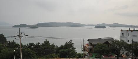 Una carretera costera con un paso de peatones, un pequeño edificio con techo verde y vista al mar con islas distantes.