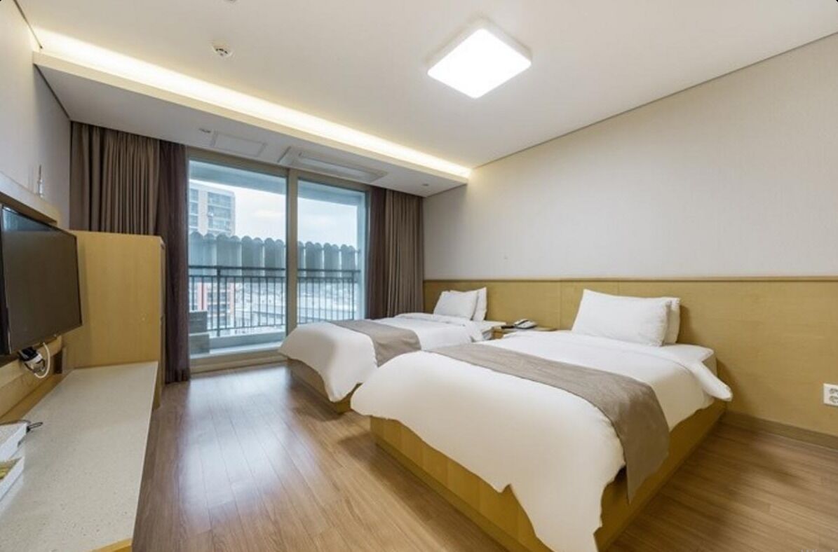 Habitación de hotel con dos camas, televisor y balcón con vista a la ciudad.