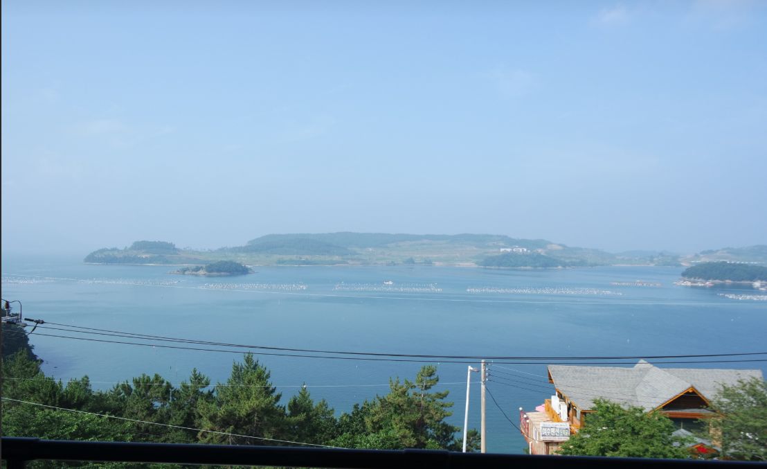 Vista costera con cielo despejado, una isla distante y un edificio con un letrero.