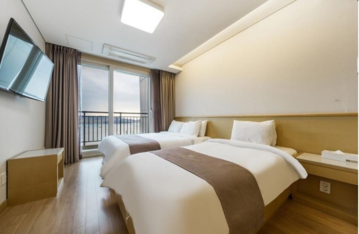 Une chambre d’hôtel avec deux lits, un téléviseur fixé au mur, un balcon avec des rideaux et un plancher en bois.