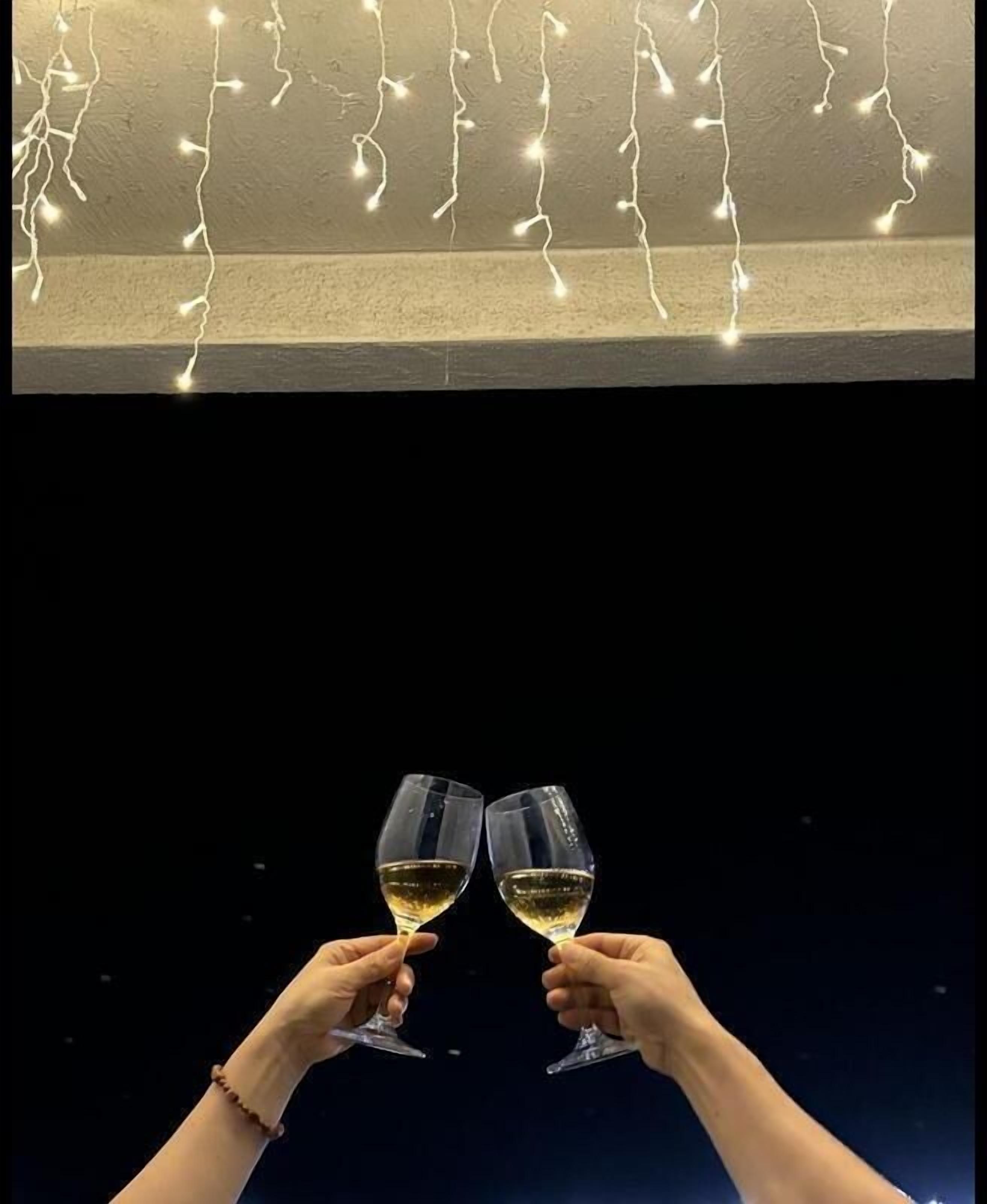 A room with a ceiling light fixture and two hands holding wine glasses.