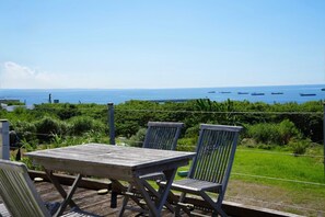 A wooden deck with a table and chairs overlooking a sea with several boats.