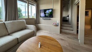 A modern living room with a sofa, a TV mounted on the wall, and a wooden coffee table. - Private Villa with Ocean Views | Churaumi & JUNGLIA | BBQ & Fireworks | Sleeps 9 (本部町)
