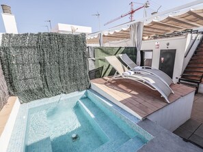 Un espace piscine aménagé sur le toit, comprenant une petite piscine, des chaises longues et un escalier menant à un niveau supérieur.