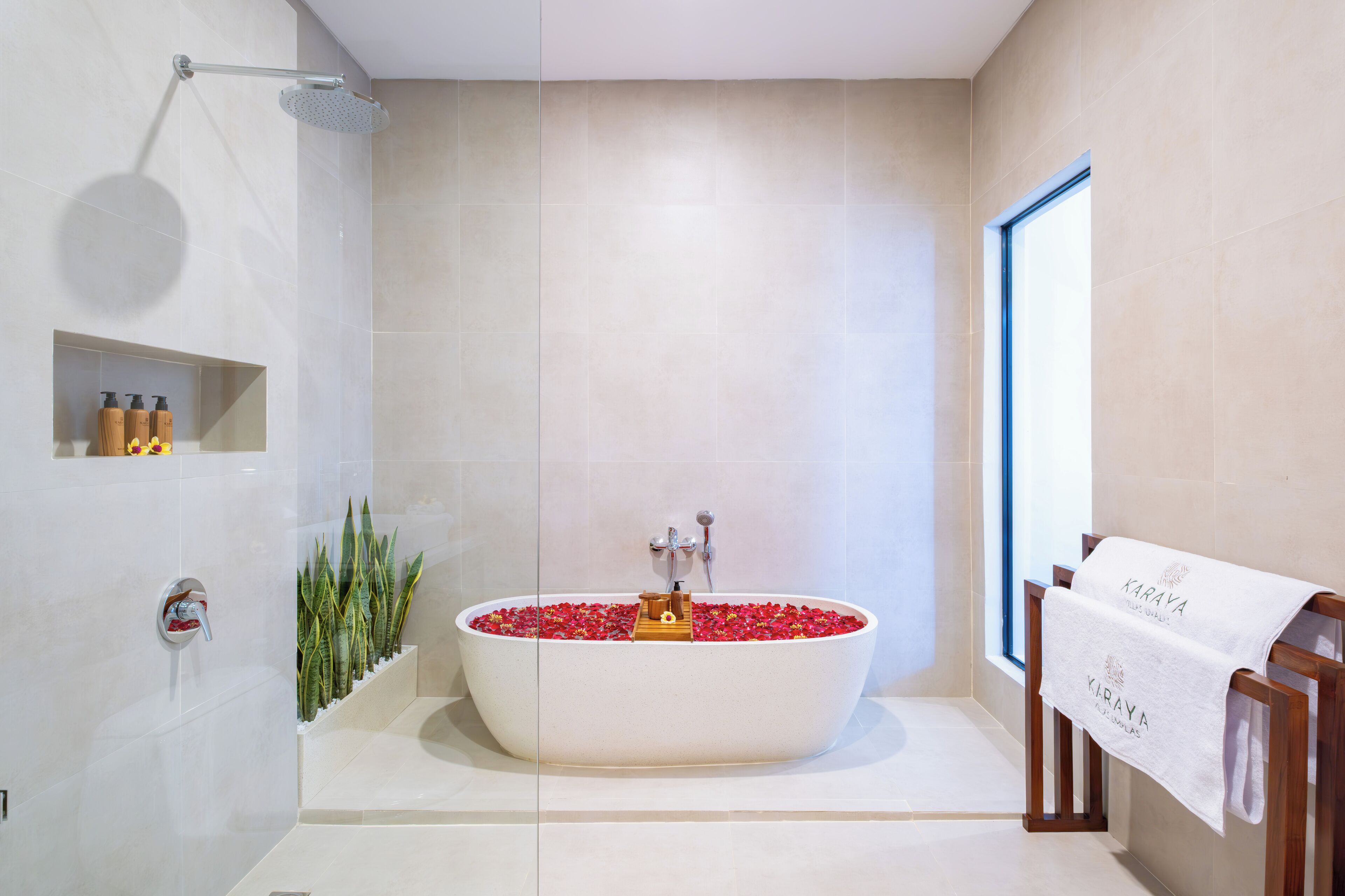 Ein modernes Badezimmer mit einer freistehenden Badewanne, gefüllt mit roten Blumen, einer Duschbrause und einem Handtuchhalter mit einem Handtuch.