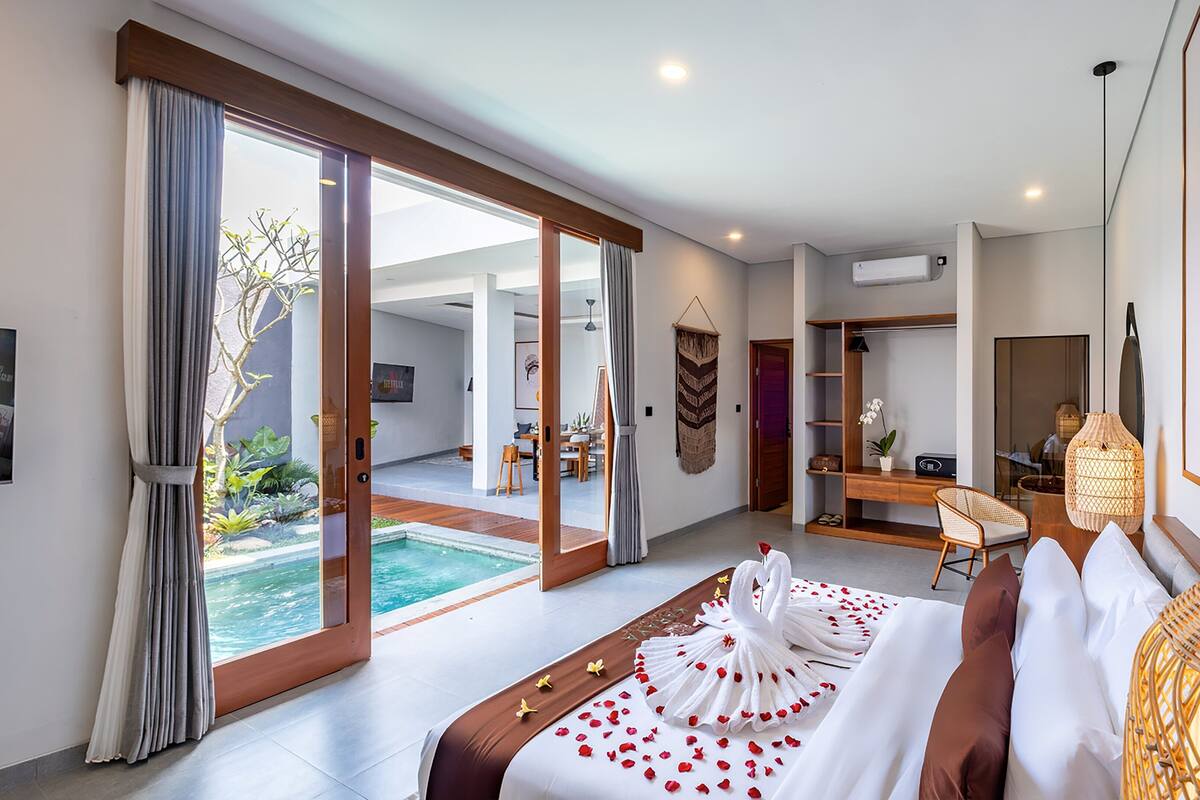A modern hotel room with a large bed, a desk, a chair, and a view of a swimming pool.
