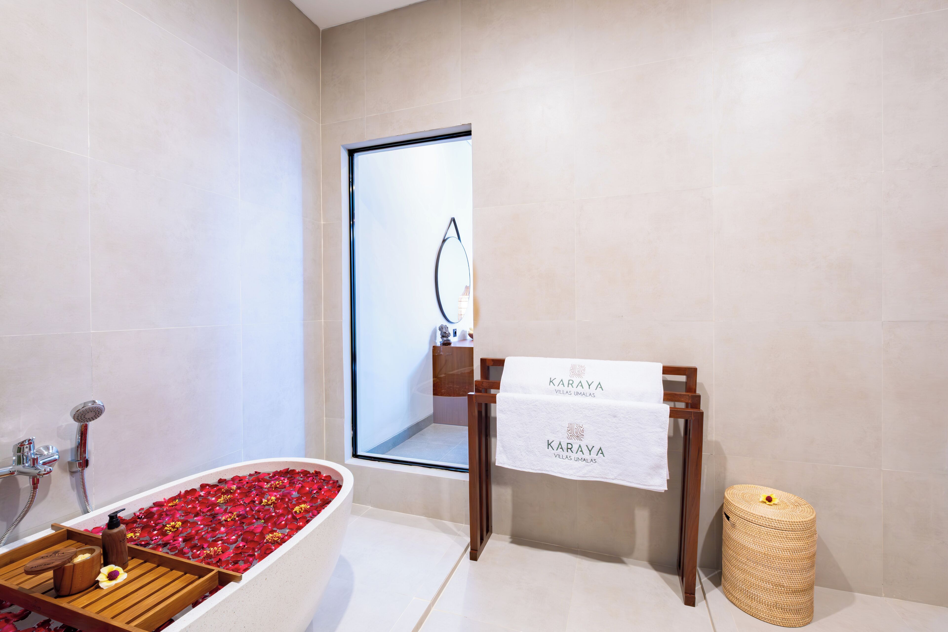 A modern bathroom with a bathtub filled with rose petals, a wooden bench, a wooden stool, and a towel rack with a towel.