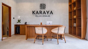 Un espace d’accueil avec un bureau en bois, deux fauteuils en osier, un ordinateur portable et une étagère ornée d’objets décoratifs.