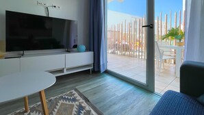 A modern living room with a flat-screen TV, a white entertainment unit, a round table, and a patterned rug. - Poolside Paradise by Best Holidays Fuerteventura (Corralejo)