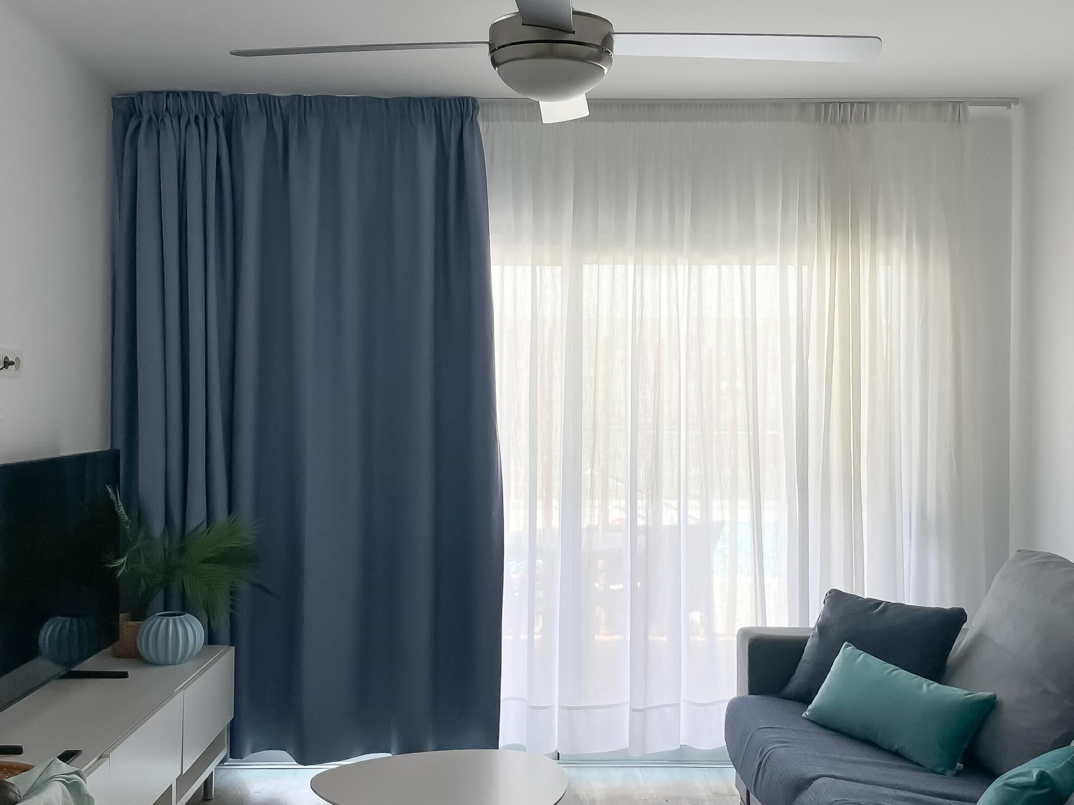 Ett modernt vardagsrum med en platt-TV, en soffa med kuddar, ett soffbord och en takfläkt.