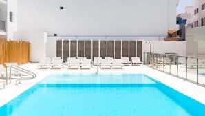 A modern indoor swimming pool with clear blue water, surrounded by white lounge chairs and a wooden fence. - Poolside Paradise by Best Holidays Fuerteventura (Corralejo)
