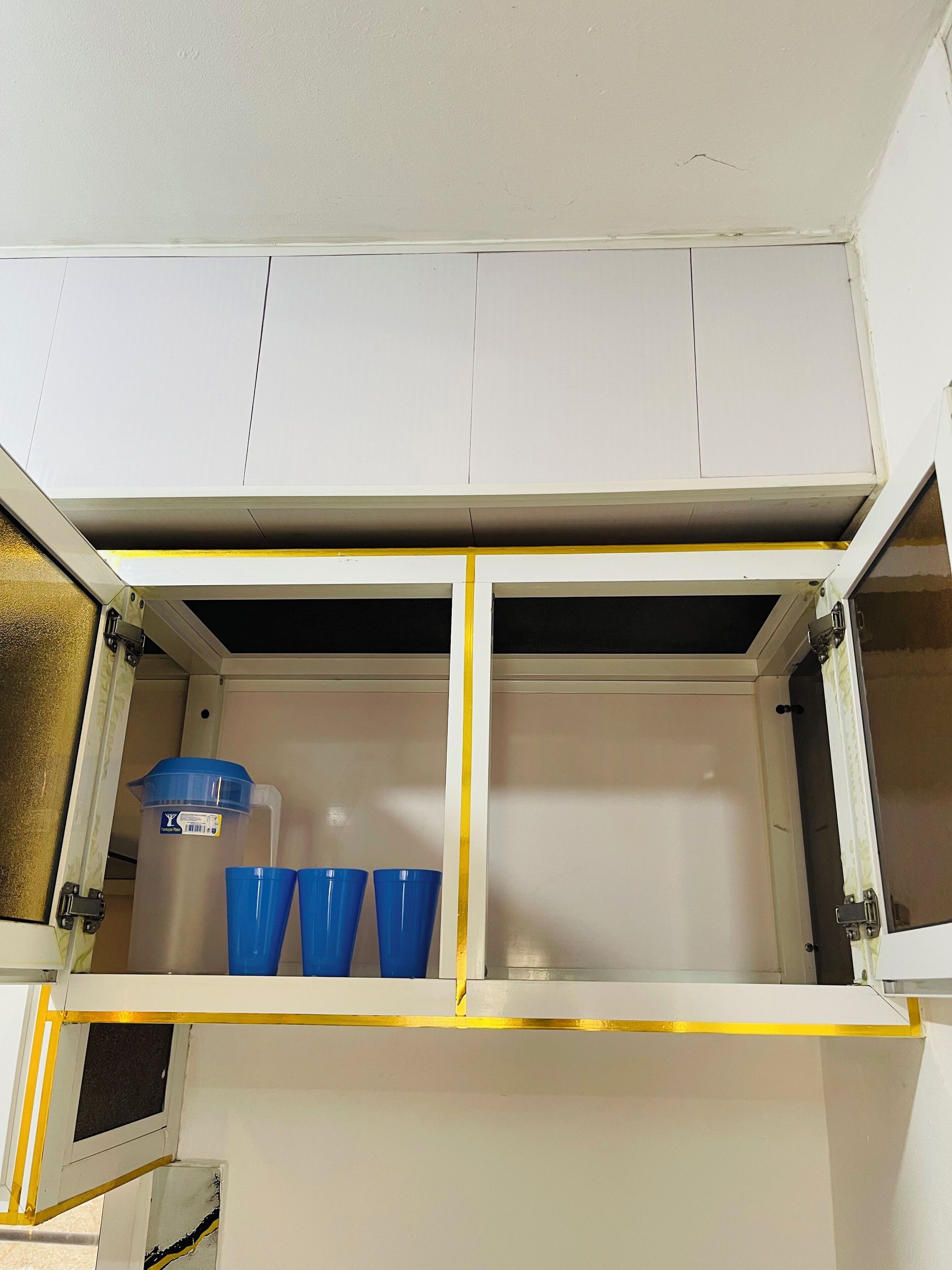 Ein weißes Schrankschrank mit gelber Einfassung, der einen blauen Behälter und zwei blaue Tassen enthält.