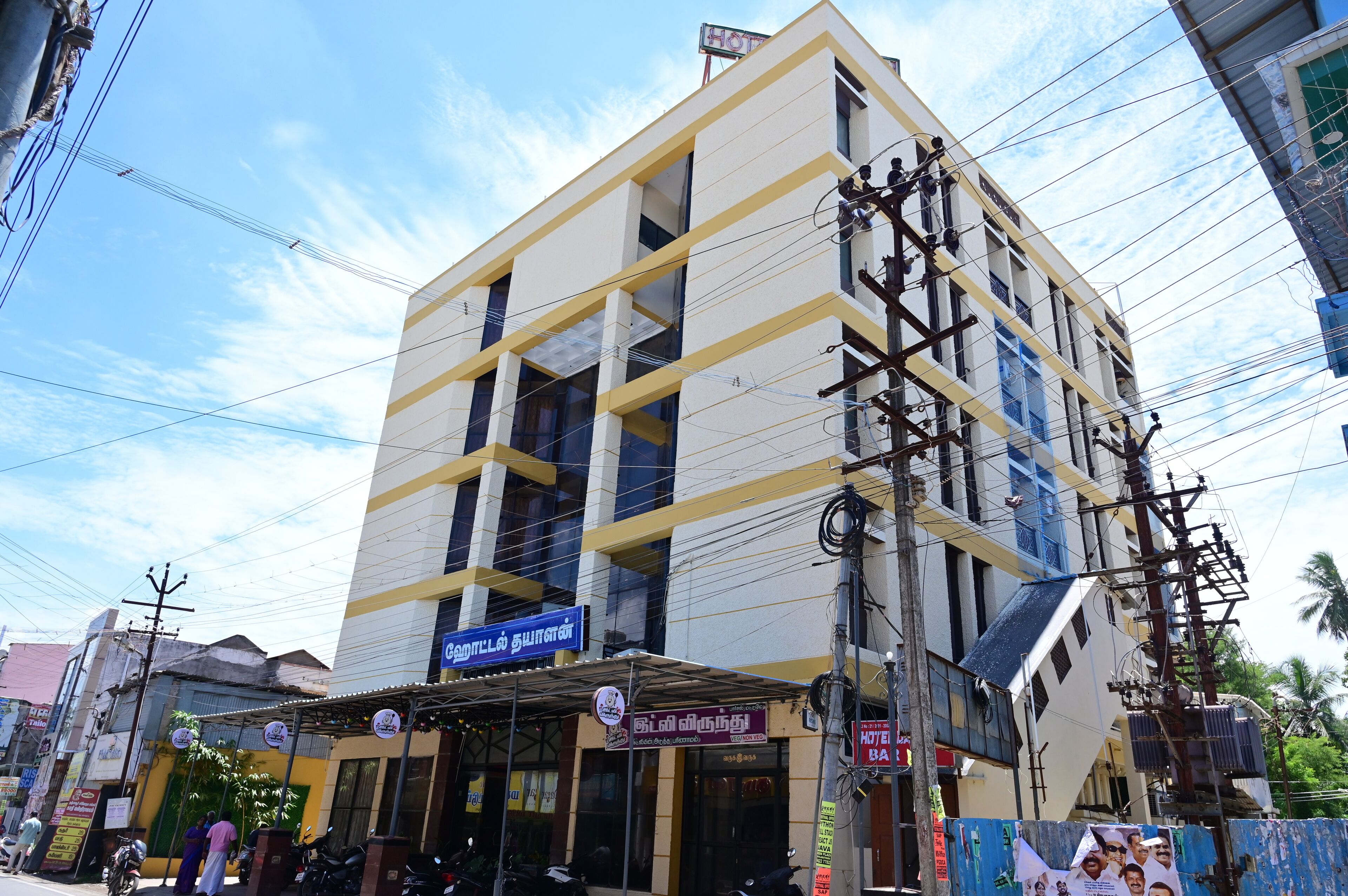 A multi-story hotel with a yellow and white facade, multiple balconies, and a sign indicating vegetarian options.