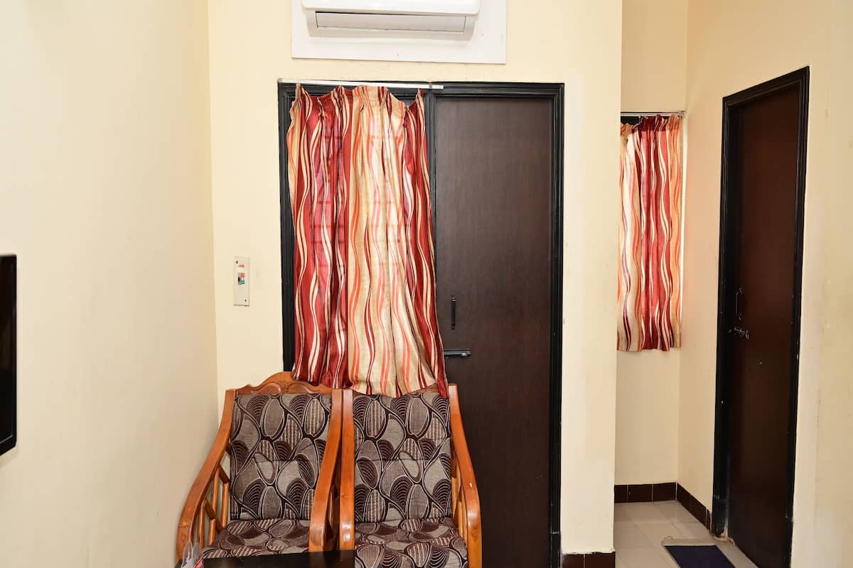 A hotel room with a bed, a wooden chair, a small table, an air conditioner, and a door with striped curtains.