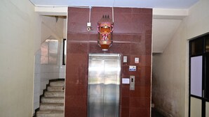 An elevator with a metallic finish, a wall-mounted decorative item above it, and a staircase to the left. - Hotel Dhayalan (Mayiladuthurai)