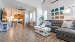 A modern living room with a grey sofa, a white coffee table, and a dining area with wooden chairs. - Hawaiian Pakele-Ocean View Estate (Waianae)