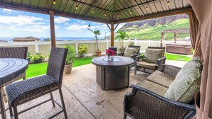 A covered patio with wicker furniture, a round table, and a view of the ocean. - Hawaiian Pakele-Ocean View Estate (Waianae)