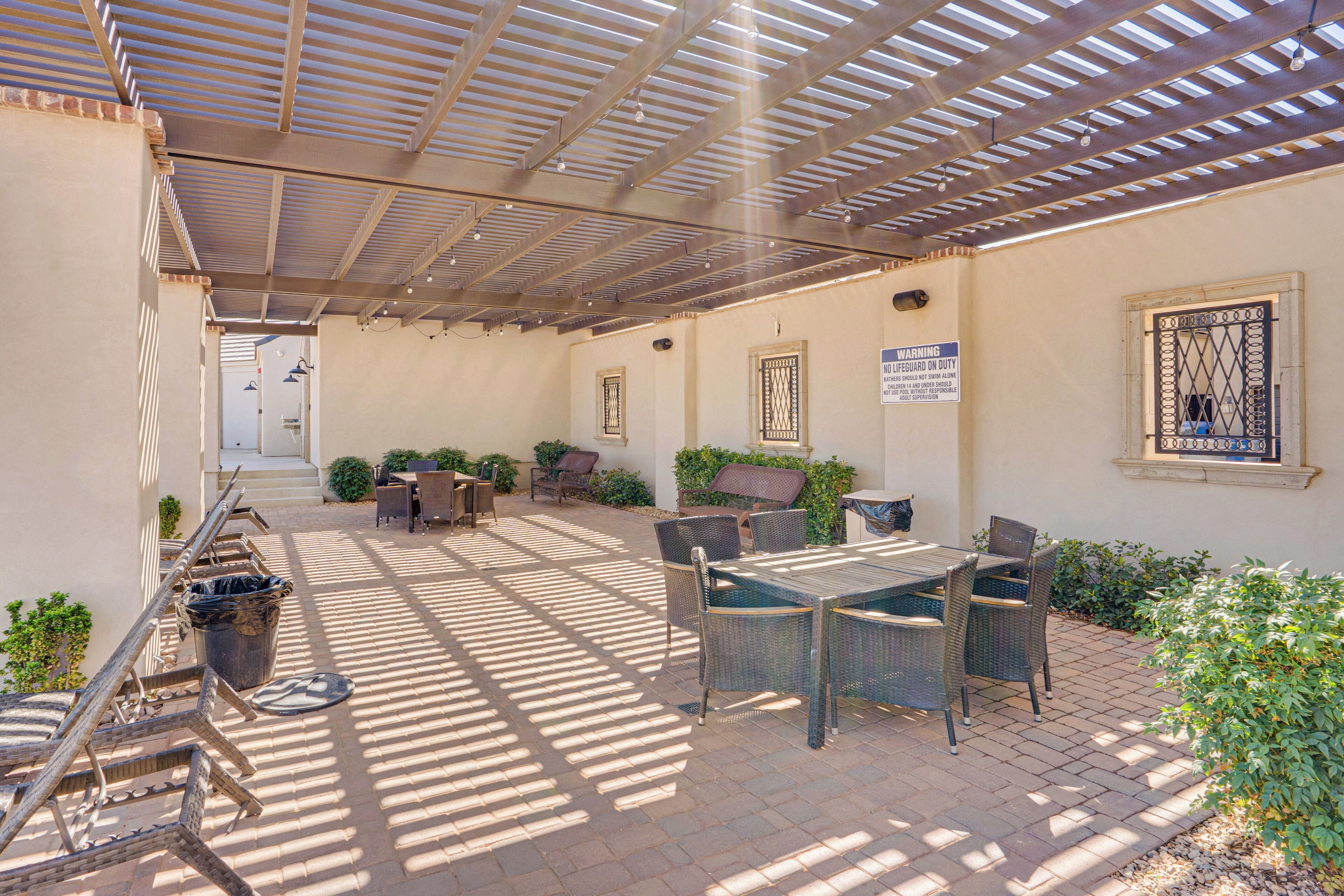 An outdoor patio area with a covered seating arrangement, a table, and chairs.